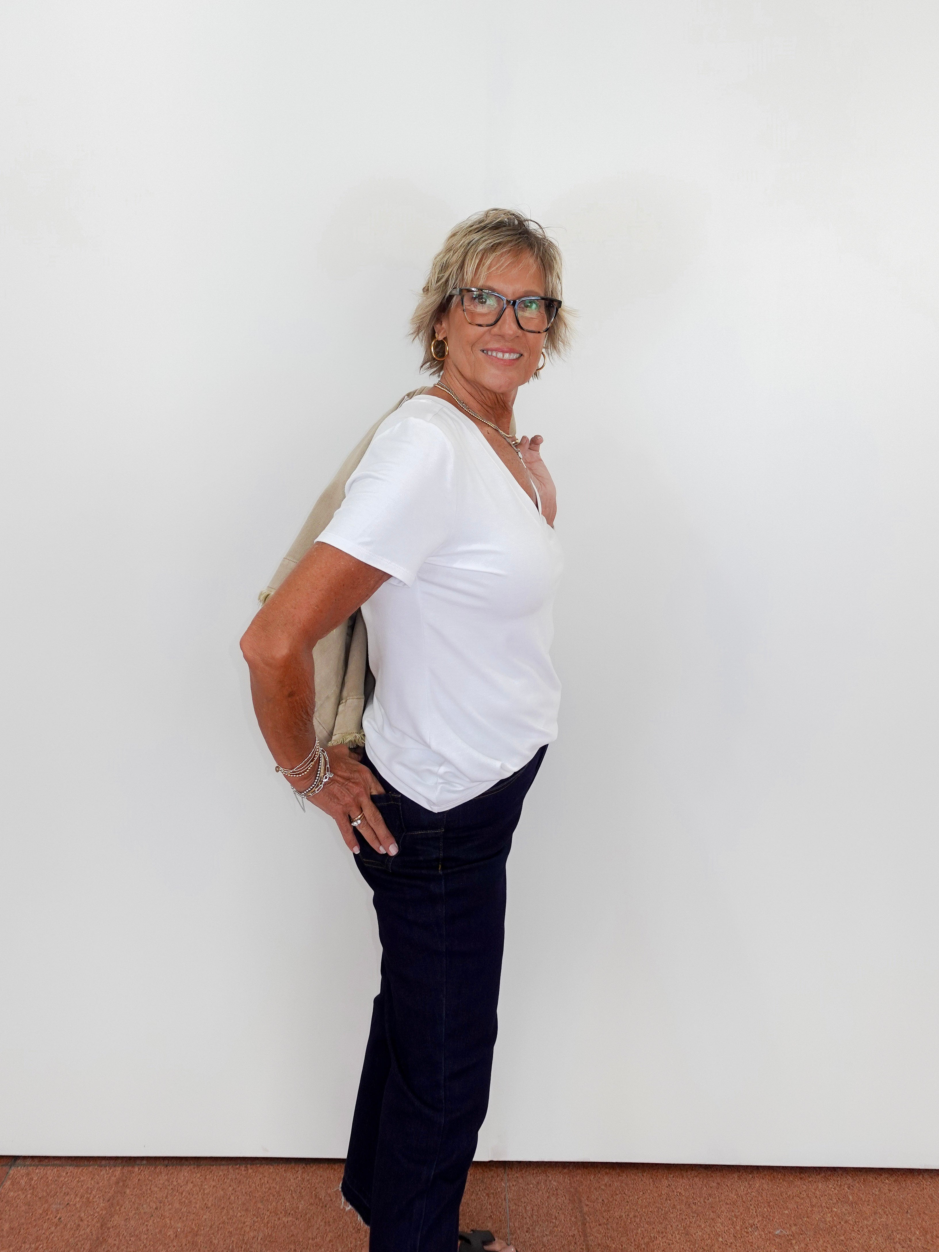 Woman wearing a white t-shirt and dark pants against a plain white wall.