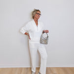 Person wearing a white outfit with a gray handbag against a plain background
