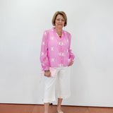 Woman wearing a pink floral blouse and white pants against a white wall.