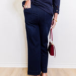 Person wearing navy blue pants and a dark shirt, holding a red handbag against a white wall.