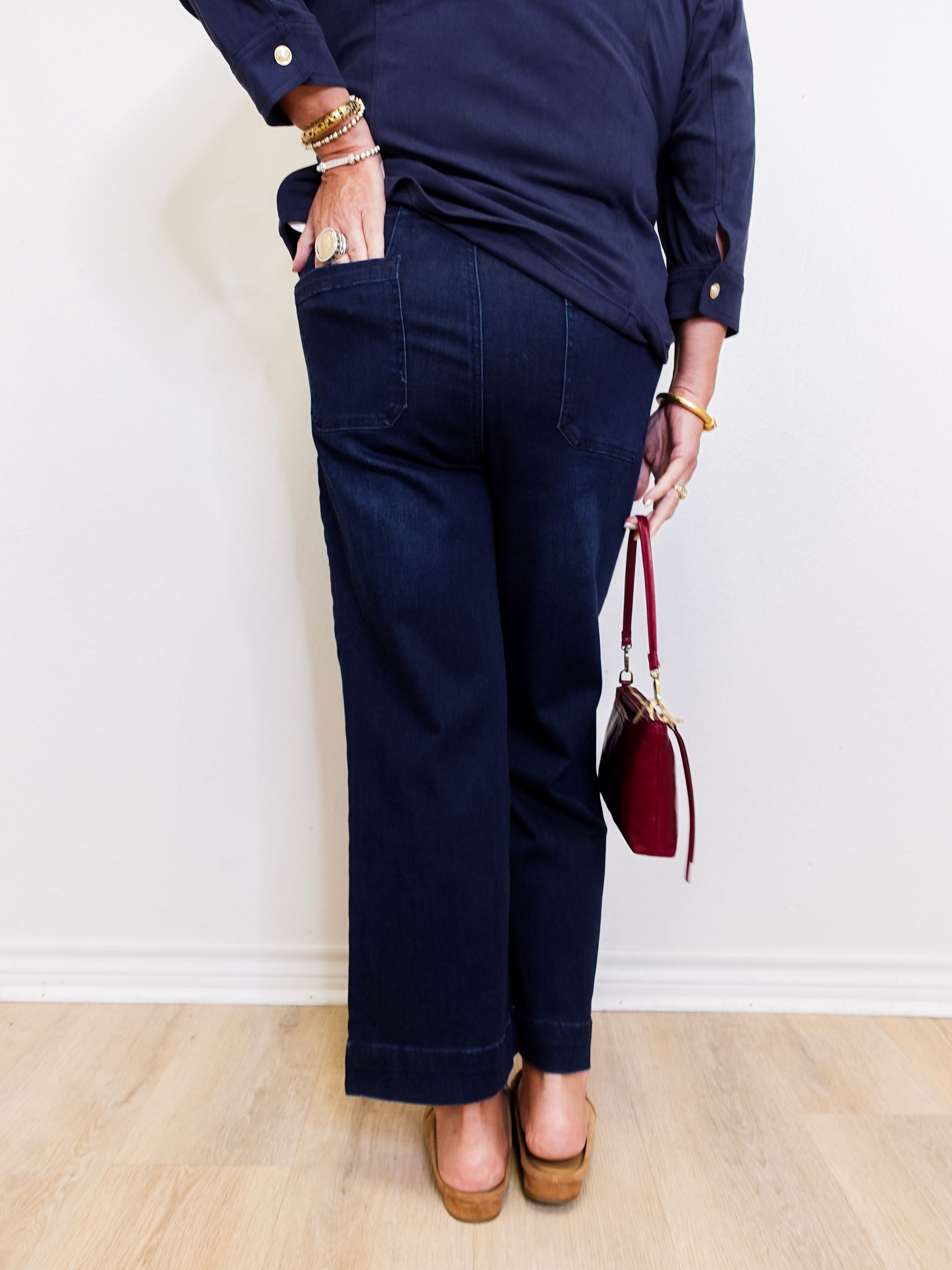 Person wearing navy blue pants and a dark shirt, holding a red handbag against a white wall.