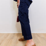 Person wearing navy pants and brown loafers on a light wooden floor.