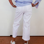 Person wearing a blue and white striped shirt with rolled-up sleeves, white pants, and white sneakers on a plain background.