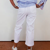 Person wearing a blue and white striped shirt with rolled-up sleeves, white pants, and white sneakers on a plain background.