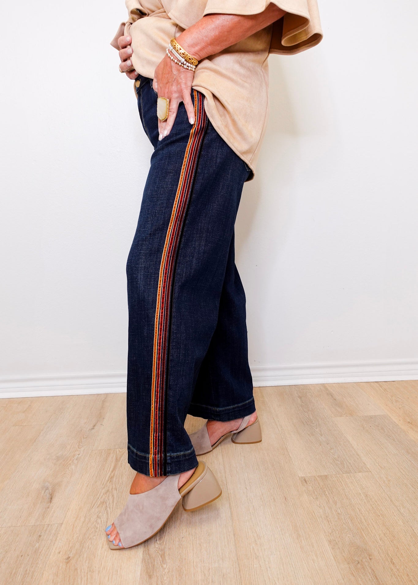 Person wearing dark blue jeans with a striped pattern on a light wooden floor.