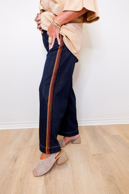 Person wearing dark blue jeans with a striped pattern on a light wooden floor.