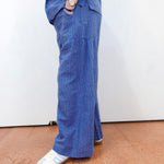 Person wearing blue overalls standing on a brown floor with a white wall background