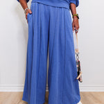 Person wearing a blue outfit with wide-leg pants against a white wall.