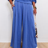 Person wearing a blue outfit with wide-leg pants against a white wall.