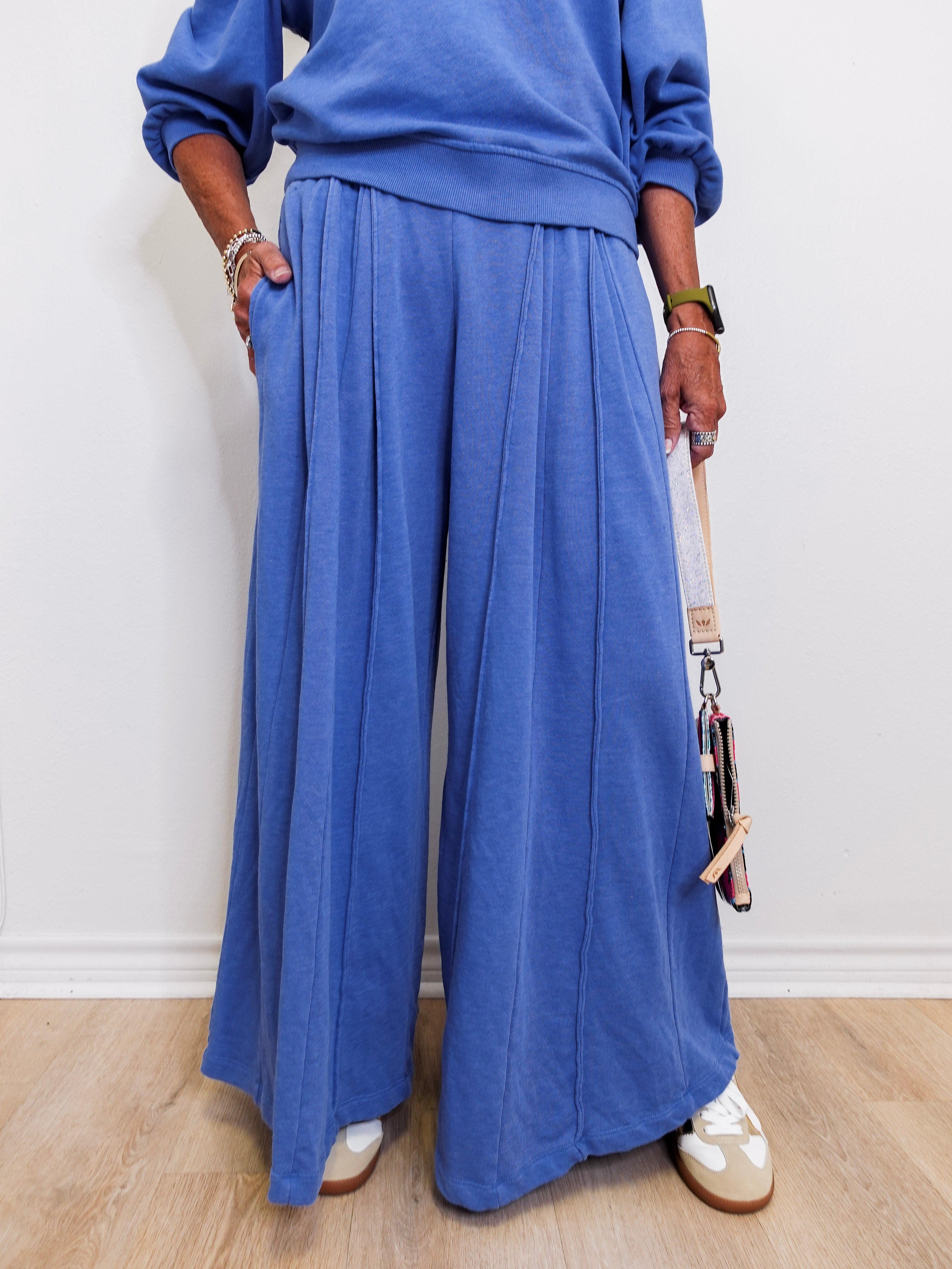 Person wearing a blue outfit with wide-leg pants against a white wall.