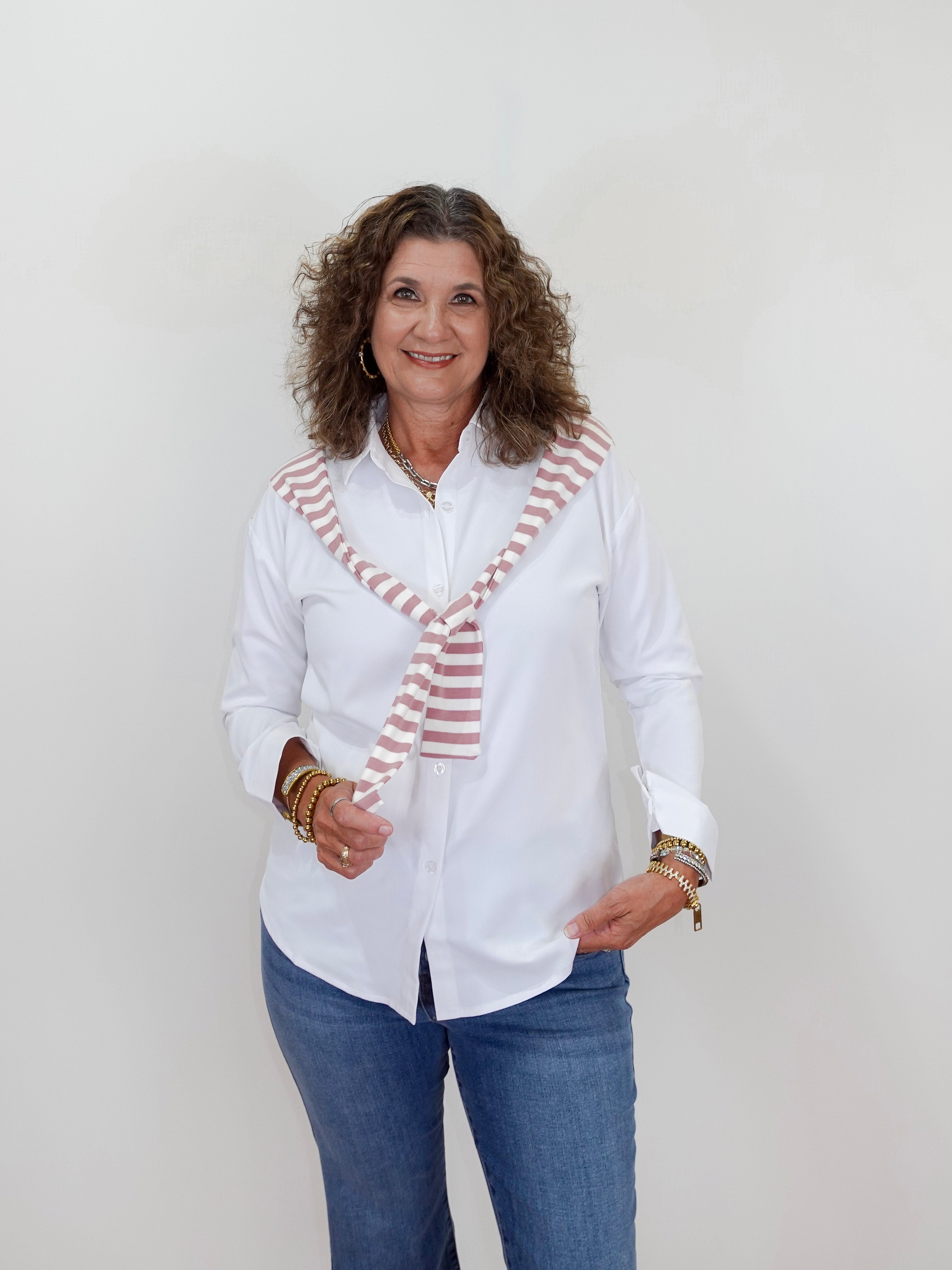 Woman wearing a white blouse with a striped tie and blue jeans against a plain background