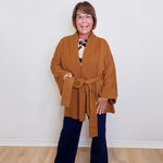Woman wearing a brown cardigan, patterned top, and dark jeans against a white background