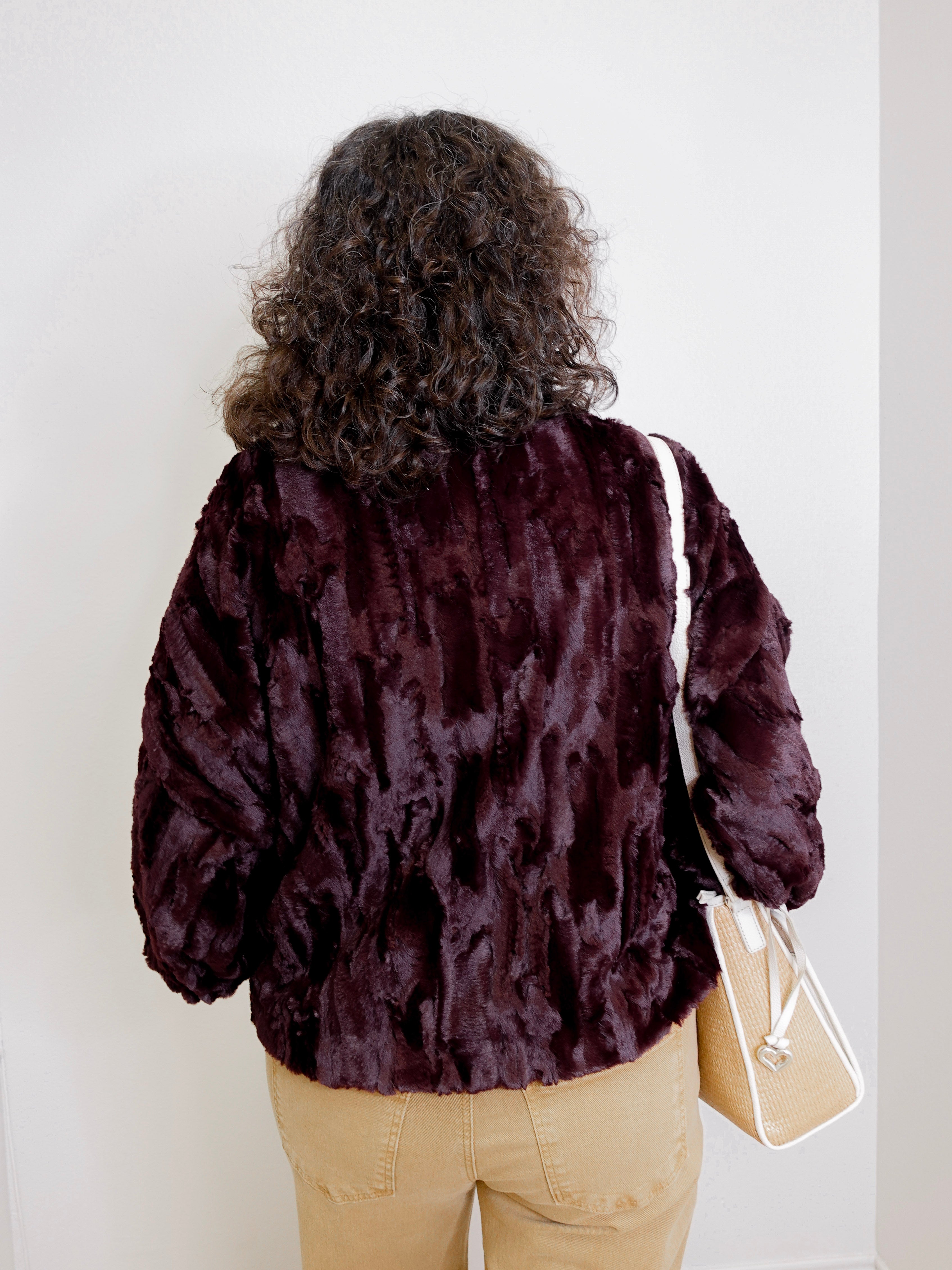 Person wearing a dark brown faux fur jacket against a white background