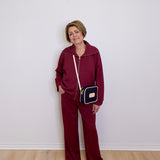 Person wearing a burgundy tracksuit with a black and gold handbag against a white wall.