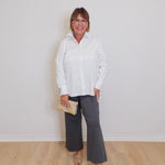 Woman wearing a white blouse and gray pants against a plain background