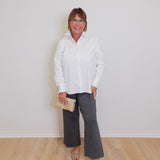 Woman wearing a white blouse and gray pants against a plain background