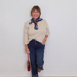 Woman wearing a beige sweater, blue jeans, and brown loafers against a white wall.