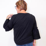 Person wearing a black top with embroidered sleeves against a white background