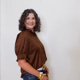 Woman wearing a brown blouse and blue jeans against a white wall