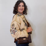 Woman wearing a gold jacket with a floral print on it, holding a brown bag against a white background. 