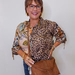 Woman wearing a leopard print top and holding a brown handbag against a white background