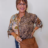 Woman wearing a leopard print top and holding a brown handbag against a white background