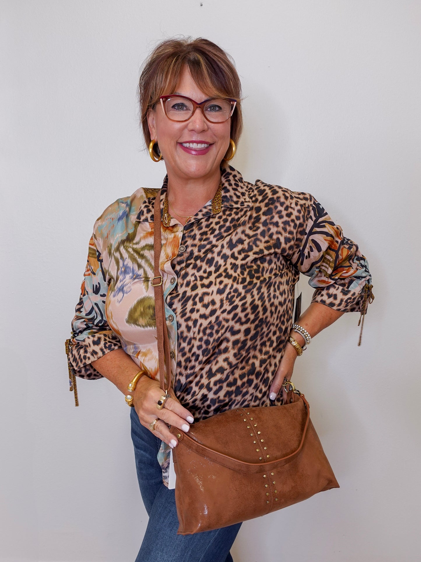 Woman wearing a leopard print top and holding a brown handbag against a white background