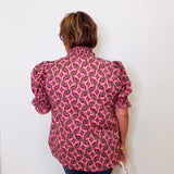Person wearing a pink patterned blouse against a white wall