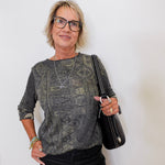 Woman wearing a patterned top and black pants, holding a black handbag against a white background