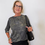 Woman wearing a patterned top and black pants, holding a black handbag against a white background