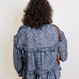 Person wearing a blue patterned blouse with a plain background