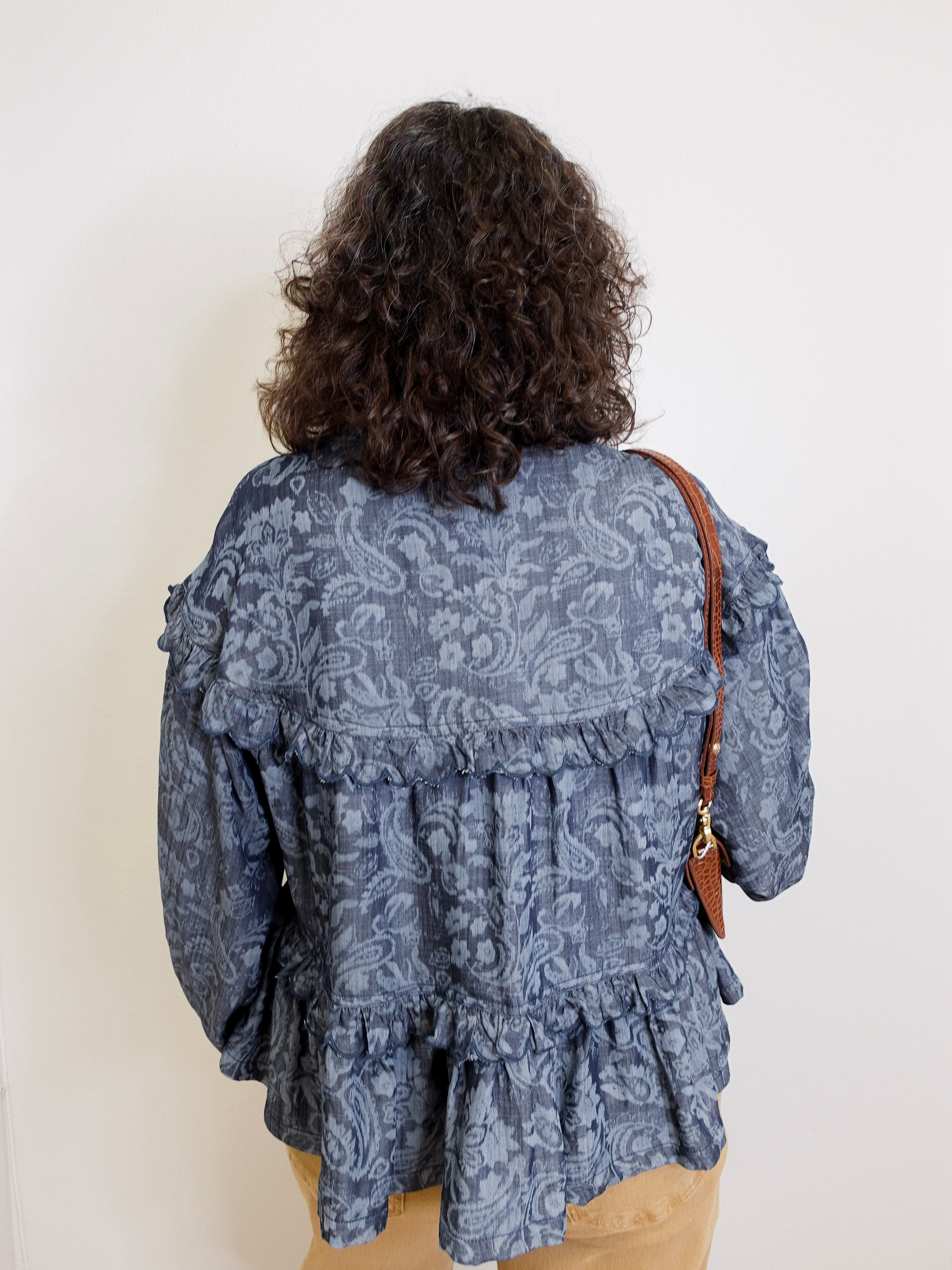Person wearing a blue patterned blouse with a plain background