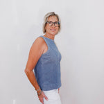 Woman wearing a blue sleeveless top and white pants against a plain background