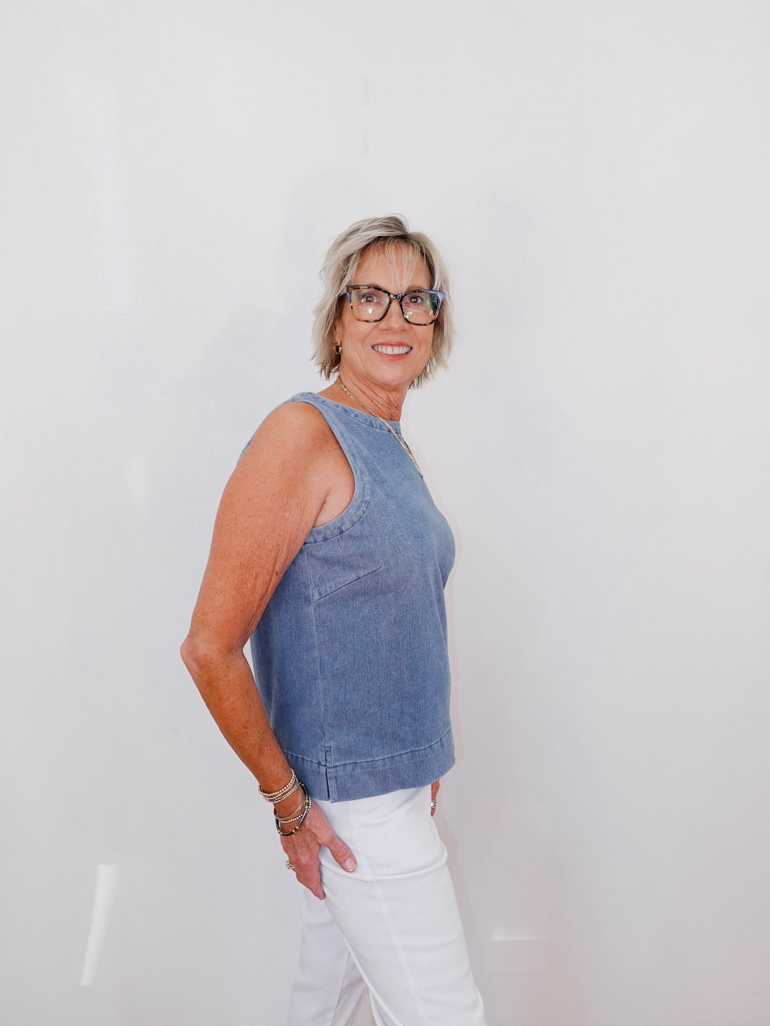 Woman wearing a blue sleeveless top and white pants against a plain background