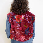 Person wearing a red floral vest over a denim jacket on a white background
