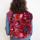Person wearing a red floral vest over a denim jacket on a white background