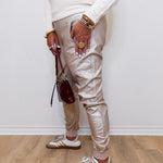 Person wearing beige pants, white sneakers, and multiple bracelets on a light wooden floor.