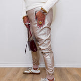 Person wearing beige pants, white sneakers, and multiple bracelets on a light wooden floor.