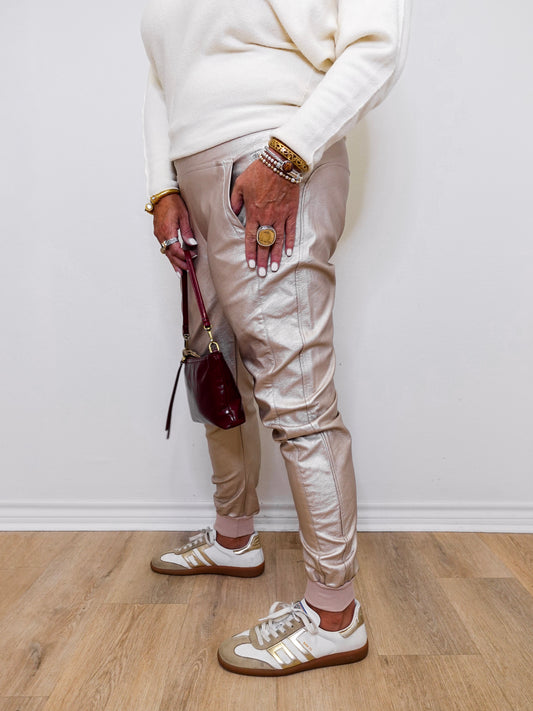 Person wearing beige pants, white sneakers, and multiple bracelets on a light wooden floor.