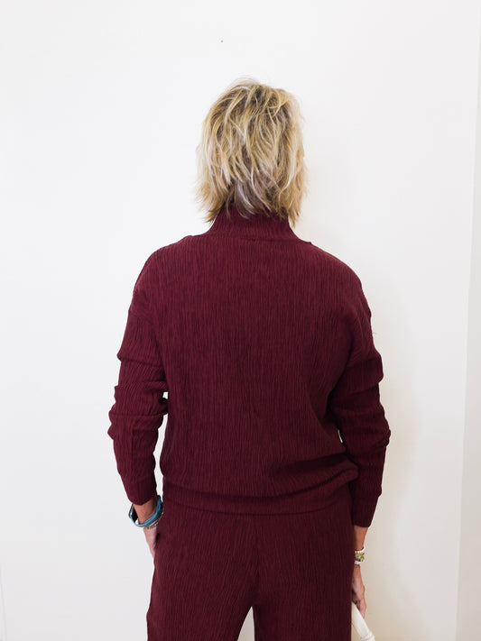 Person wearing a maroon sweater and pants against a white background