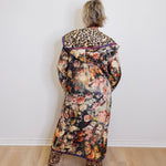 Person wearing a floral coat with leopard print accents against a white wall.