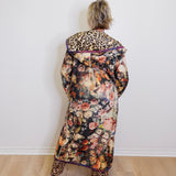 Person wearing a floral coat with leopard print accents against a white wall.