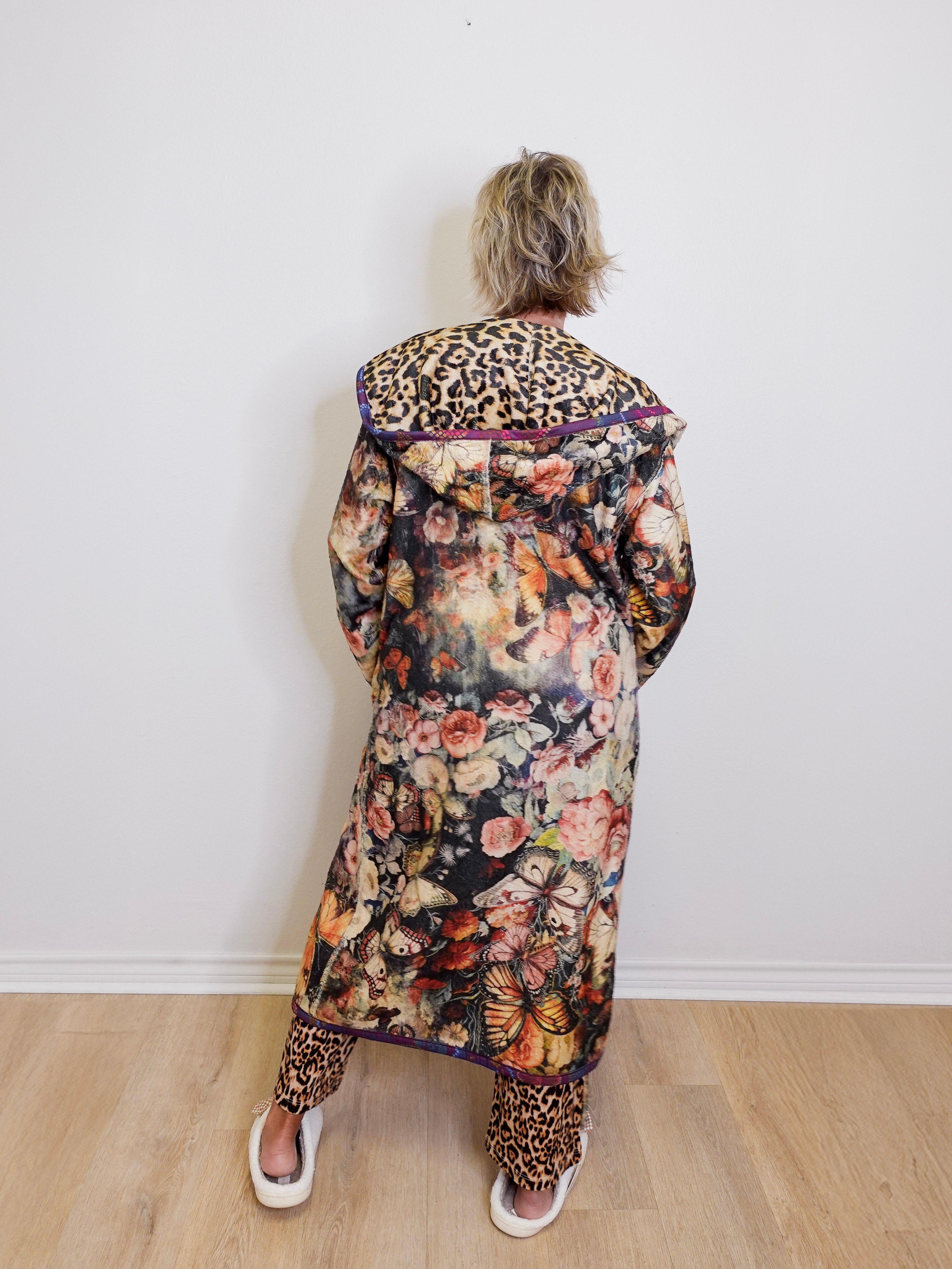 Person wearing a floral coat with leopard print accents against a white wall.