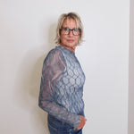 Person wearing a textured gray sweater and blue jeans against a plain background