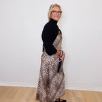 Woman wearing a black turtleneck and leopard print dress against a white wall.