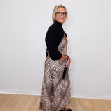 Woman wearing a black turtleneck and leopard print dress against a white wall.
