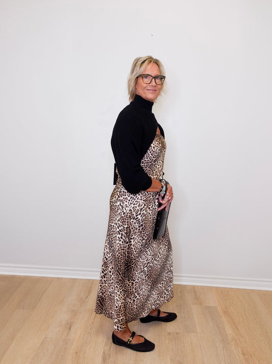 Woman wearing a black turtleneck and leopard print dress against a white wall.