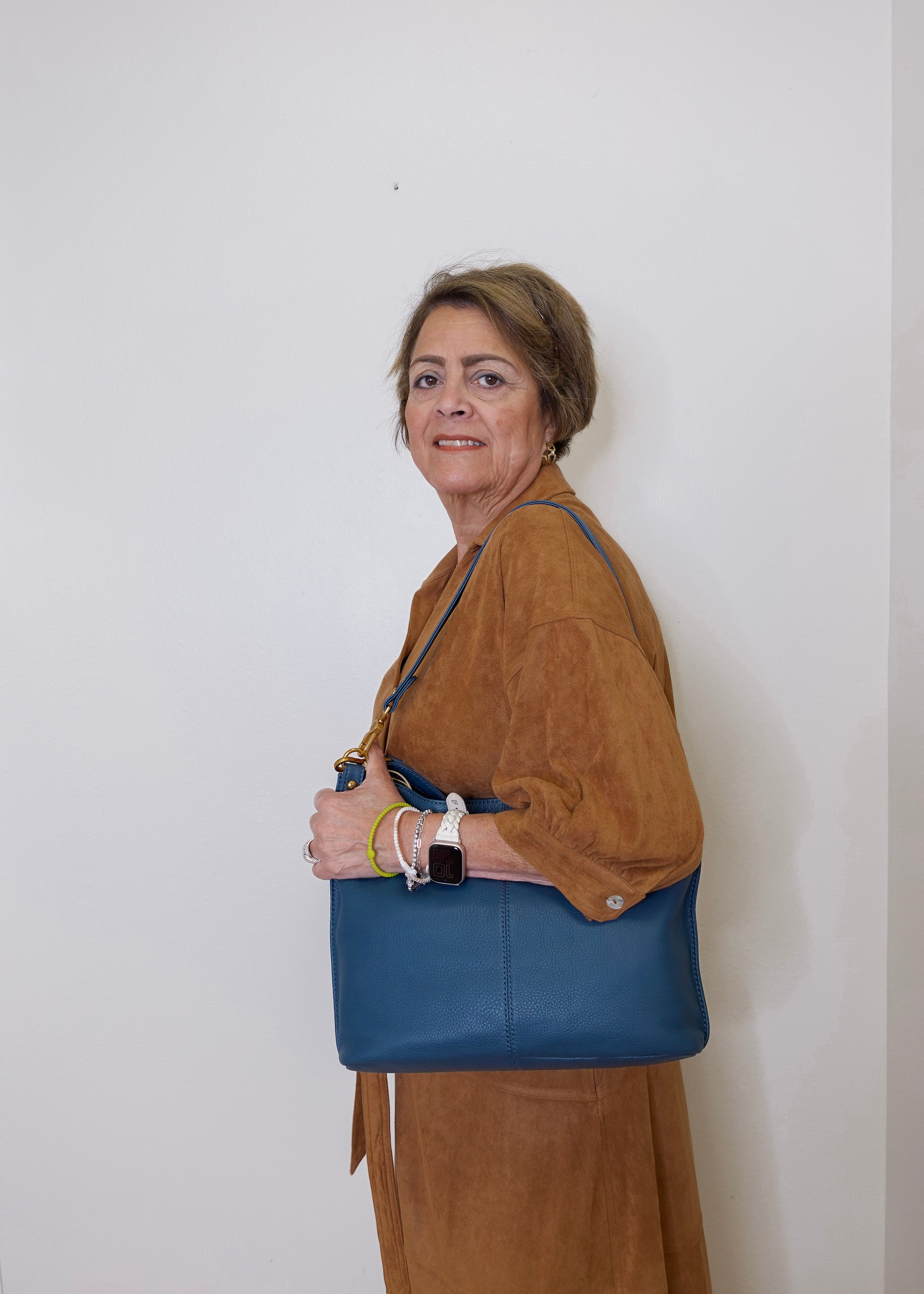 Woman holding a blue handbag against a white wall