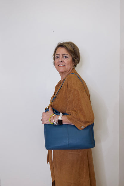 Woman holding a blue handbag against a white wall