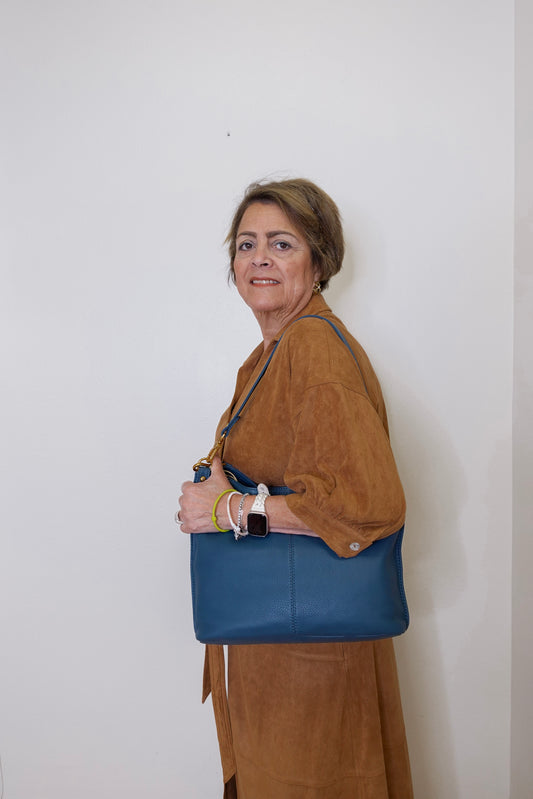 Woman holding a blue handbag against a white wall